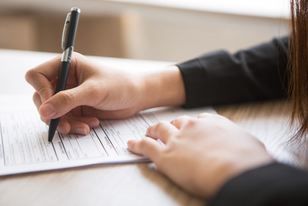 woman holding pen and filling in application form at table