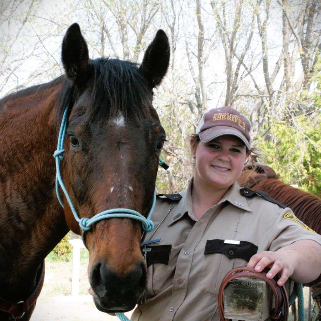 Woman in a Sheriff's Posse uniform standing next to a horse
