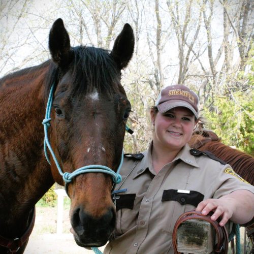 Woman in a Sheriff's Posse uniform standing next to a horse