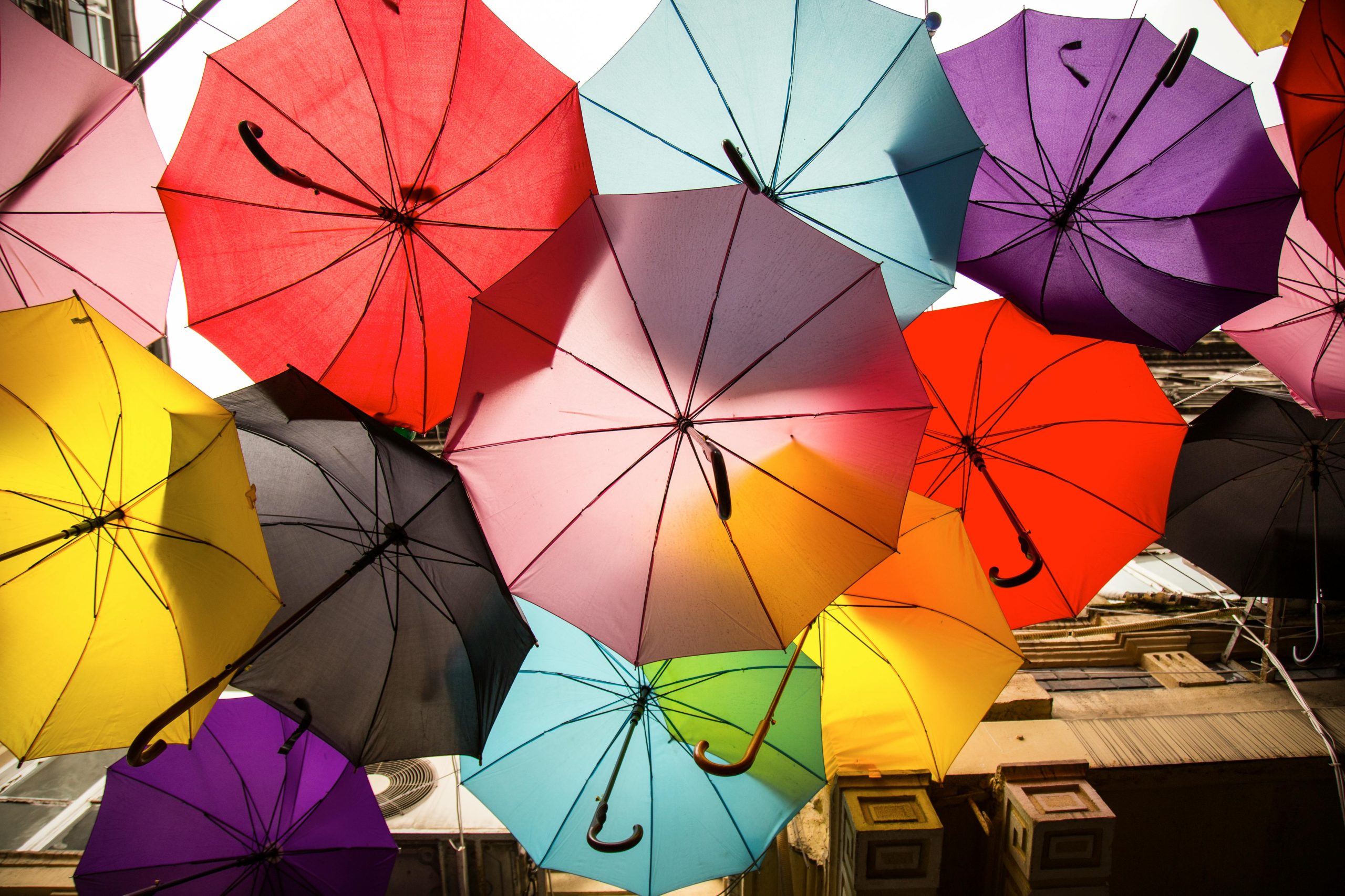 A dynamic array of colorful umbrellas creates a vibrant canopy in this lively outdoor street scene.