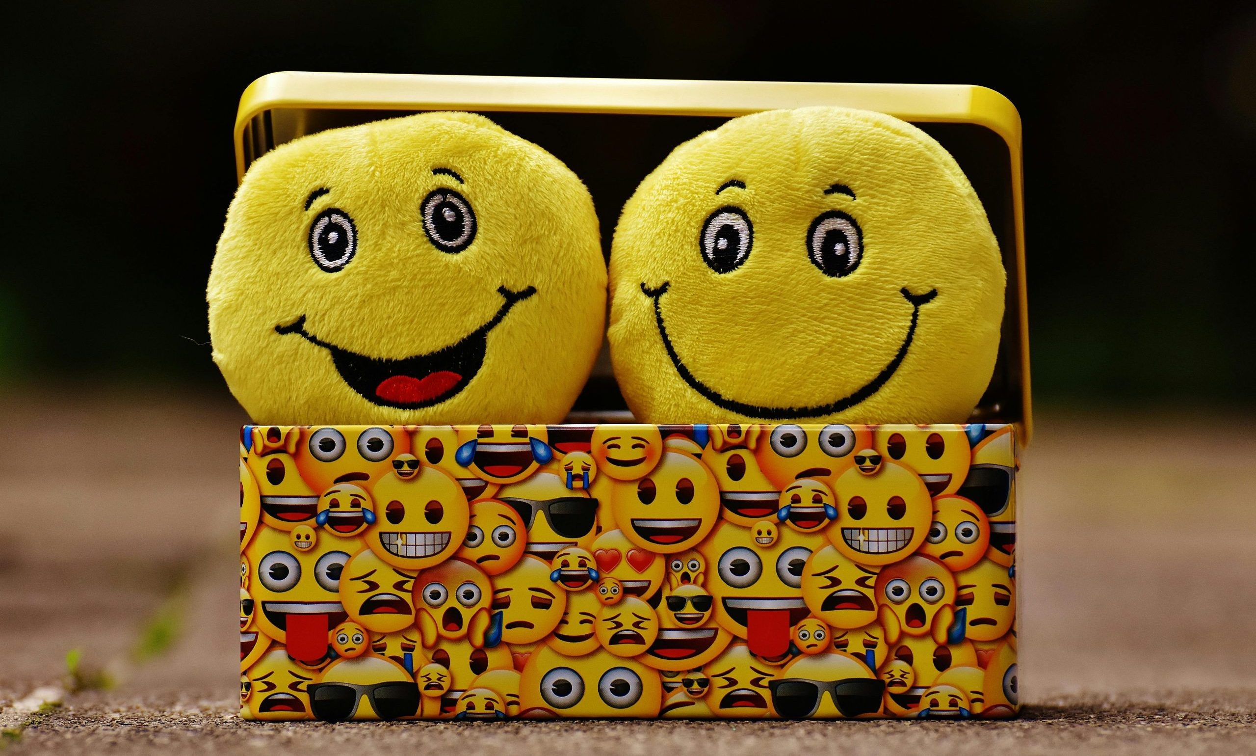 Two yellow smiley plush toys in an emoji-themed box, expressing fun and happiness.