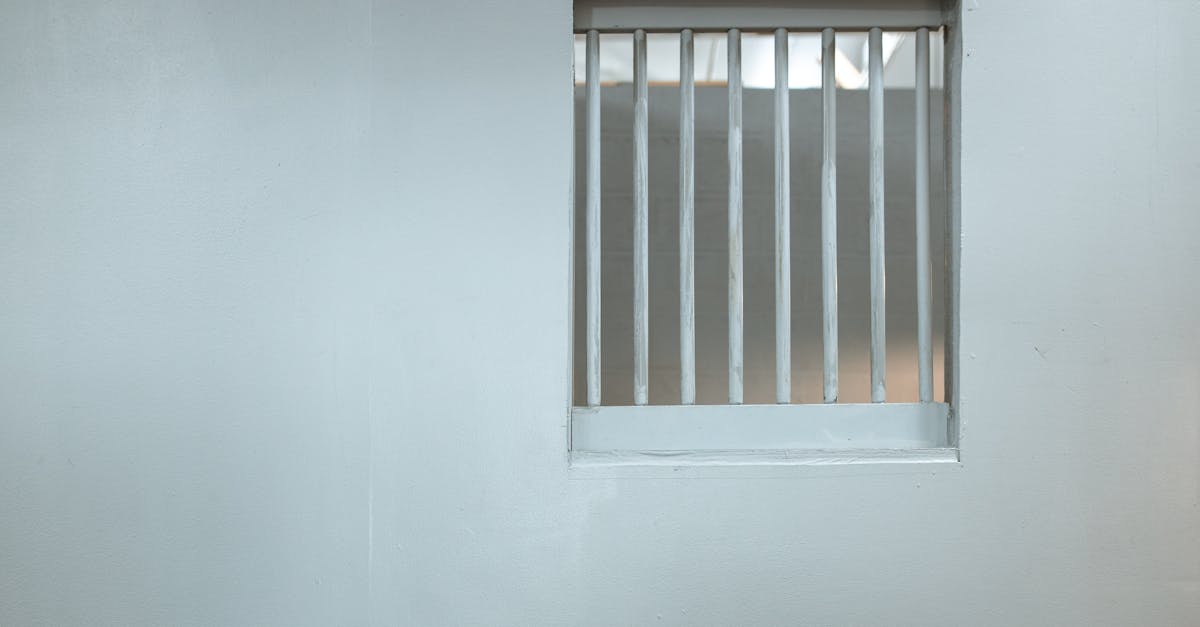 A minimalist white wall featuring a small barred window, symbolizing confinement.