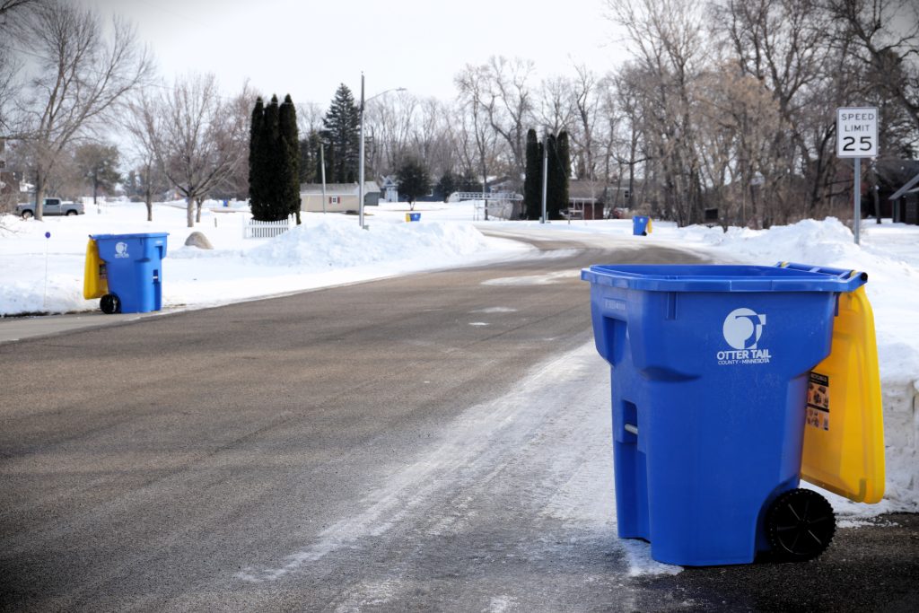 Blue and yellow recycling bins lined up along a street in the winter
