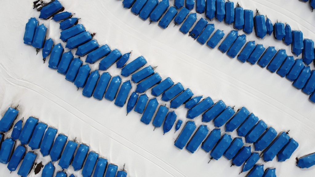 Aerial view of boats wrapped in blue plastic and sitting in a field of snow.