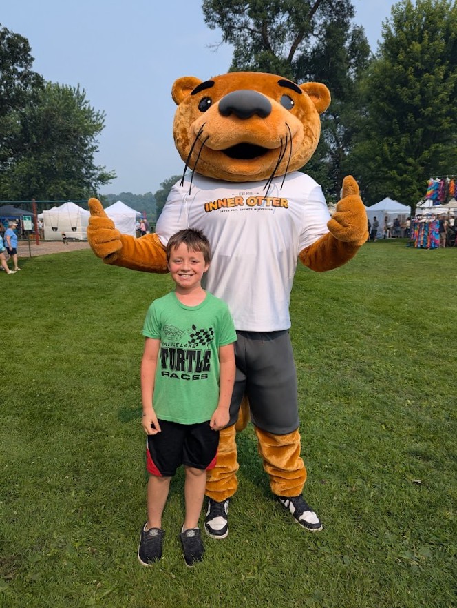 A young boy poses for a picture with the Otter Tail Country Inner Otter mascot at the Phelps Mill Festival